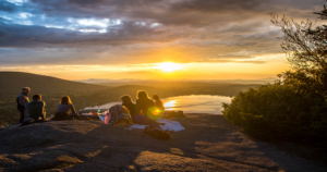Photo by Arthur Poulin on Unsplash of people having a Church picnic at sunset on a hill