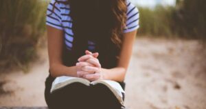 Woman with hands folded on the Bible in prayer
