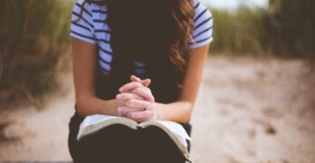 Woman with hands folded on the Bible in prayer